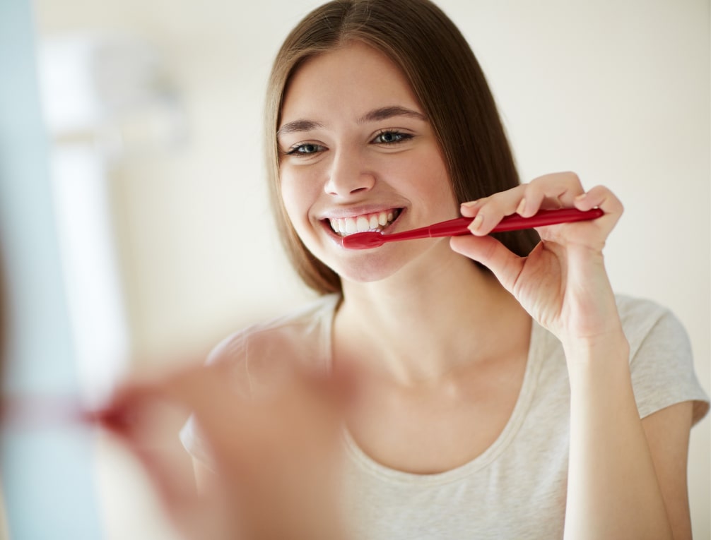 A young woman brushes her teeth with a brush and smiles