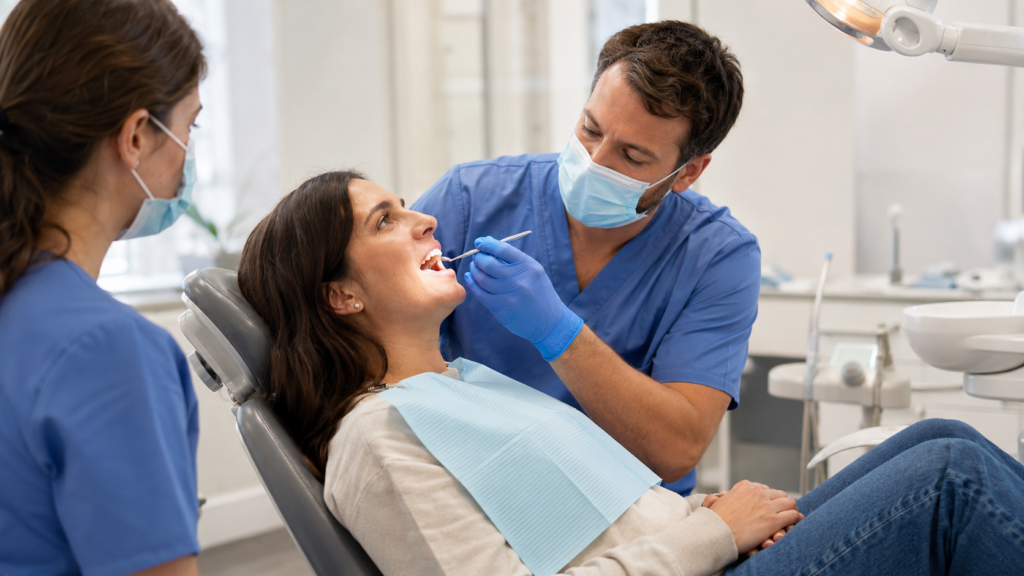 A dentist performs a gentle examination while an assistant supports an adult patient returning for dental care.
